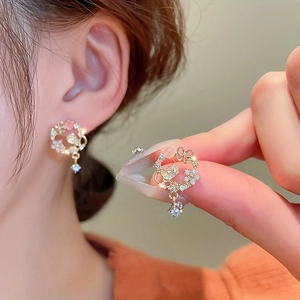 Close-up of golden floral wreath stud earring featuring pink stones and white flower petals
