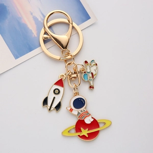 Space themed metal keychain with colorful enamel astronaut and rocket charms on a gold ring