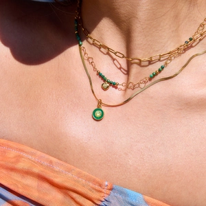 Détail d'un collier multicouche en acier doré avec perles vertes et pendentif cœur