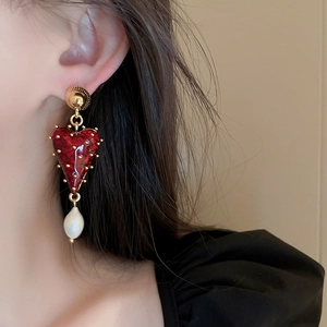 Gros plan d'un mannequin portant des boucles d'oreilles cœur rouge avec perles baroques dorées
