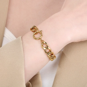 Close-up of a gold-toned chunky Cuban link bracelet worn on a wrist with a khaki blazer