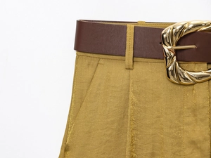 Dettaglio macro dei pantaloni in raso senape con fibbia della cintura in metallo dorato