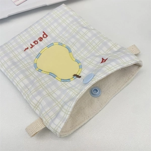 Detail of cute embroidered pear on a white plaid canvas storage bag with snap closure