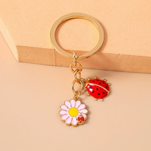 Detail of a pink daisy flower and red ladybug keychain with golden metal ring and chain