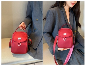 Detail view of red nylon crossbody bag with multi-zipper layers and metallic logo plate