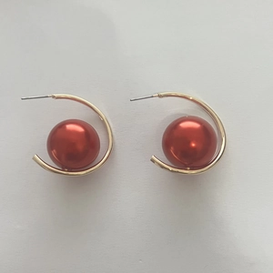 Detailed view of C-shape golden earrings with a large red pearl on a white background