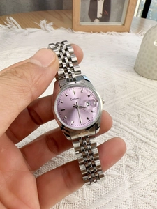 Detail of silver steel watch band with pink dial and calendar window held in hand