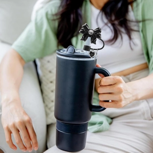 Detail of a matte black tumbler with a rhinestone bow and heart charm on the straw