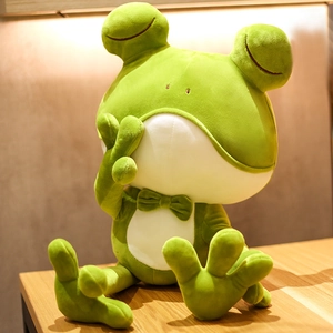 Cute green frog plush toy pillow with bow tie sitting on a wooden table surface