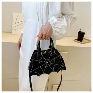 Close-up of black spider web bat wing saddle bag held by model in white dress