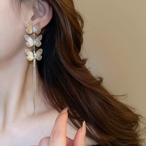 Detailed view of long gold butterfly tassel earrings with sparkling rhinestones on model