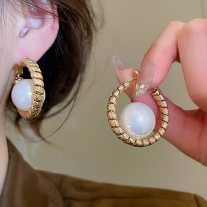 Macro detail of gold-plated hoop earrings with textured spiral finish and large pearl