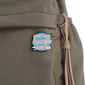 Macro shot of Earth enamel pin with text 'Destroy the Patriarchy Not the Planet' on backpack