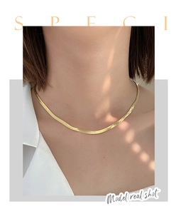 Close-up of a wide flat gold herringbone chain choker worn by a model in soft lighting