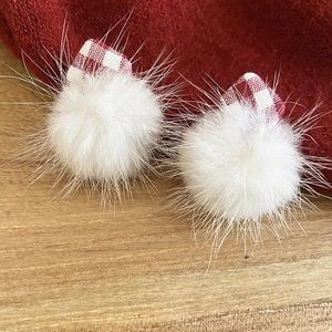 Close-up of white plush fur ball earrings with red plaid fabric detail on wood surface