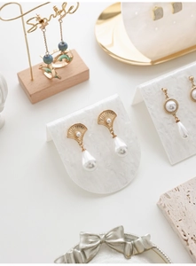 Detail of vintage gold and pearl earrings displayed on a marble textured acrylic stand