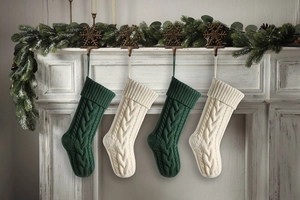 Set of four knitted Christmas stockings in green and cream hung on a fireplace