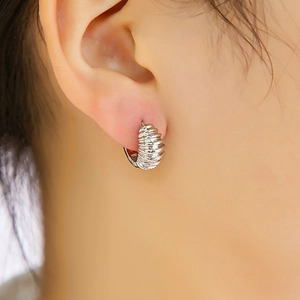Vue macro d'une boucle d'oreille créole argentée torsadée portée avec finition polie
