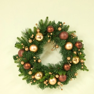 Christmas wreath with green pine needles, gold berries, and ornaments on a plain wall