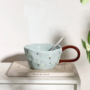Detail of light blue ceramic mug with brown handle and cute bunny pattern and metal spoon