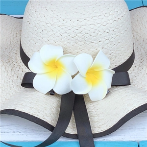 Detail of beige woven straw hat with black ribbon and plumeria floral decorations
