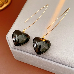 Detail of gold ear hooks with black heart pendants on a grey velvet jewelry stand