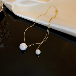 Detailed macro of gold fishtail pendant necklace with double pearls on sleek silk