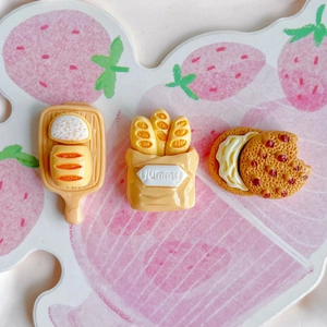 Miniature resin food charms including bread and biscuits on strawberry background