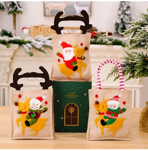 Three Christmas burlap gift bags with Santa and snowman designs in a festive setting