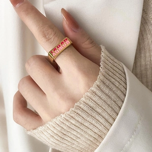 Close-up of golden square ring with pink and red enamel HONEY lettering on a hand