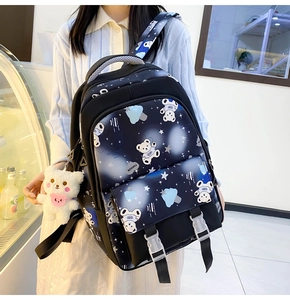 Detail of black school backpack featuring cartoon bear print and plush pendant on model