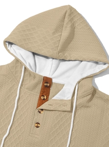 Détail d'un sweat à capuche kaki texturé avec patte à quatre boutons et cordons blancs