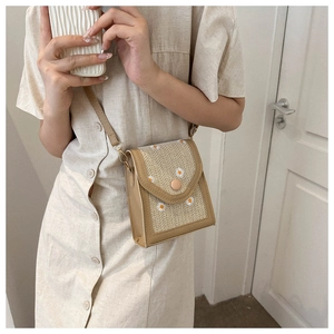 Close-up of beige straw woven bag featuring delicate white daisy embroidery and button