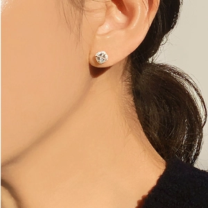 Close-up of sparkling silver zircon stud earrings with a central stone on a female model