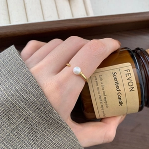 Close-up of a minimalist gold pearl ring worn by a model holding a candle