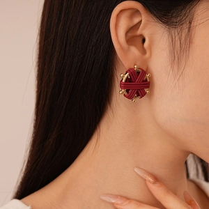 Close-up of retro burgundy woven round earrings with gold bead trim on model's ear