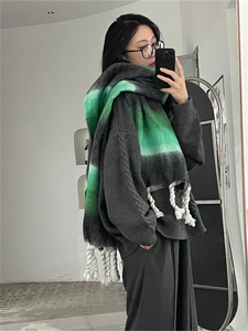 Detail of gradient grey and green thick mohair scarf with white tassels worn by a model
