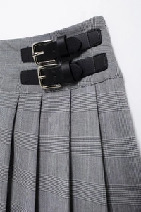 Detailed close-up of grey plaid pleated skirt featuring dual black leather buckles