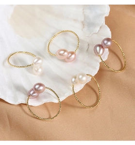 Close-up of five teardrop pearl rings on a shell with elegant silk background
