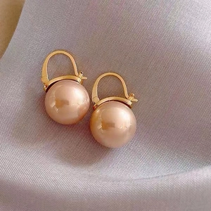 Macro view of high-gloss round champagne pearl earrings with gold-plated hooks