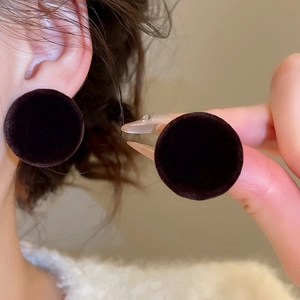 Detail of dark brown flocked velvet button stud earrings worn by a female model
