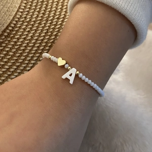 Detail shot of a handmade beaded bracelet with letter A charm and gold heart on wrist