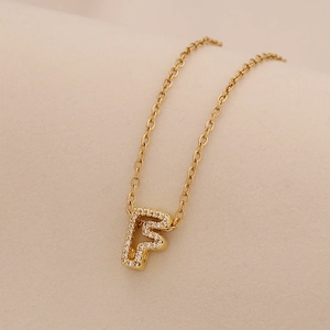 Macro shot of gold initial F pendant necklace with sparkling clear zircon pavé stones