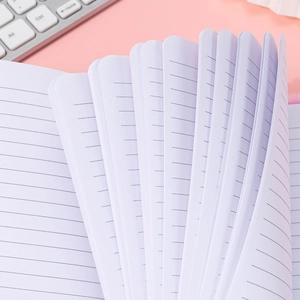 A5 cartoon notebook with lined white paper and thick pages on a pink desk background