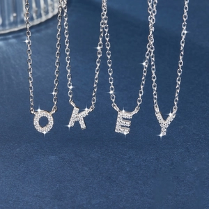 Macro shot of silver 925 necklaces with O, K, E, Y crystal pendants on a dark blue background