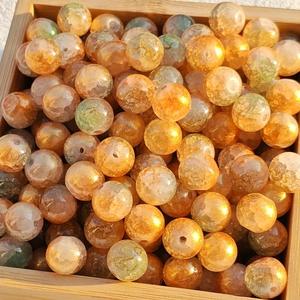 Close-up of orange glass beads with gold foil texture in a wooden tray for DIY jewelry