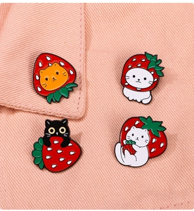 Detail shot of four cute black and ginger cat enamel pins with strawberry theme on fabric
