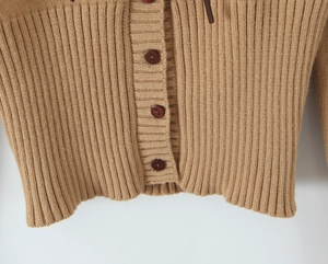 Dettaglio dell'orlo del cardigan in maglia a coste cammello con bottoni marroni scuri