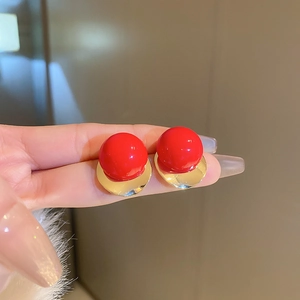 Detail showing hand holding pair of red ball earrings with shiny gold metal base studs