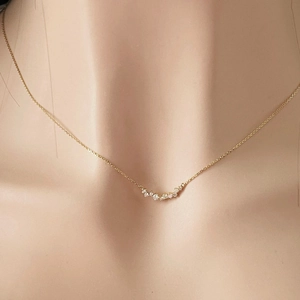 Close-up of a minimalist gold smile necklace with zircon curve on model's neckline